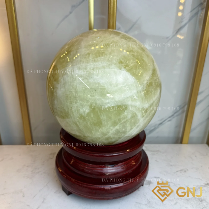 Quả Bi Cầu Đá Thạch Anh Vàng Tự Nhiên — trên đế gỗ nâu đỏ trước tủ kính, góc 1