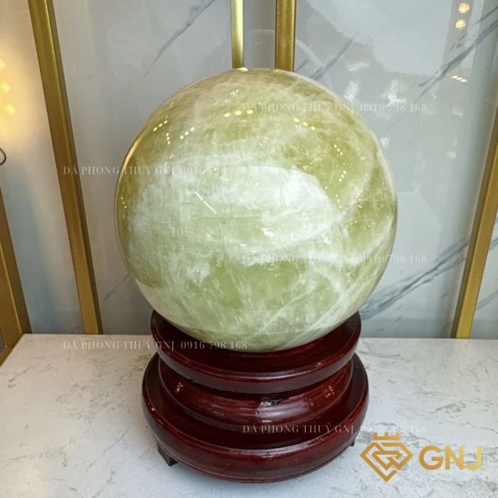 Quả Bi Cầu Đá Thạch Anh Vàng Tự Nhiên — trên đế gỗ nâu đỏ trước tủ kính, góc 2