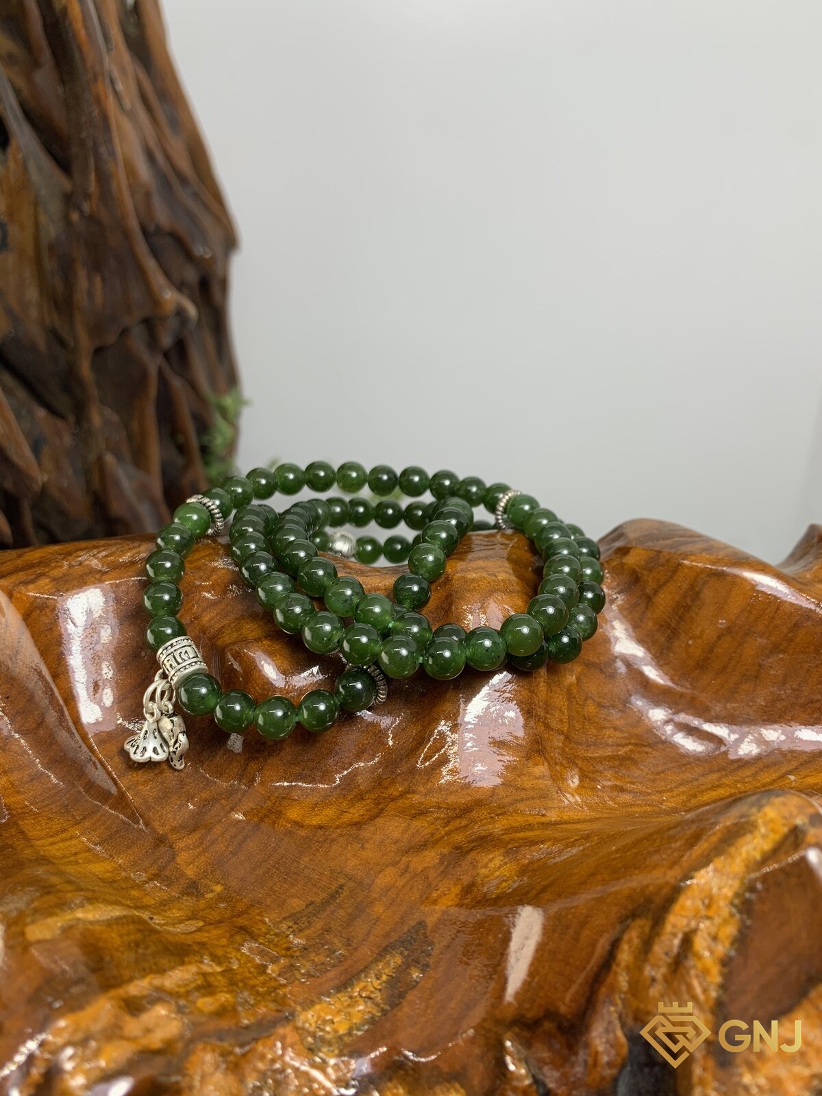 Vòng ngọc bích nephrite quấn ba vòng charm bạc — ảnh chính diện trên đế gỗ, ngọc bích tự nhiên xanh rêu