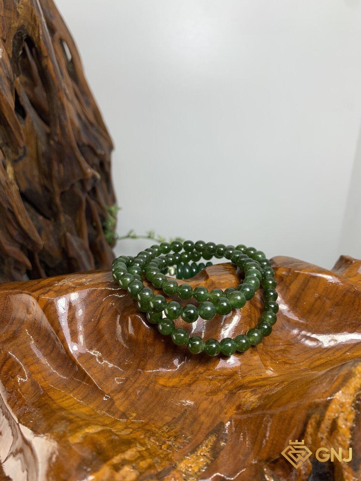 Vòng ngọc bích nephrite quấn vòng charm đồng điếu — ảnh chính diện trên đế gỗ, ngọc bích tự nhiên xanh rêu