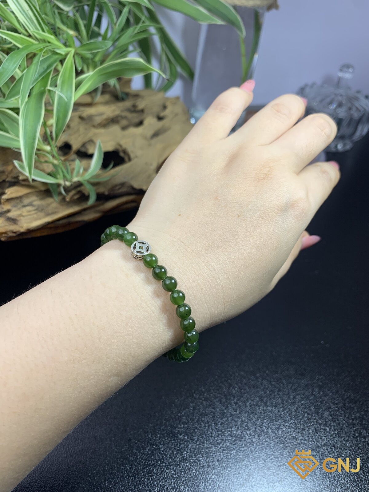 Vòng tay ngọc bích nephrite đeo trên tay, bối cảnh cây xanh và gỗ mộc