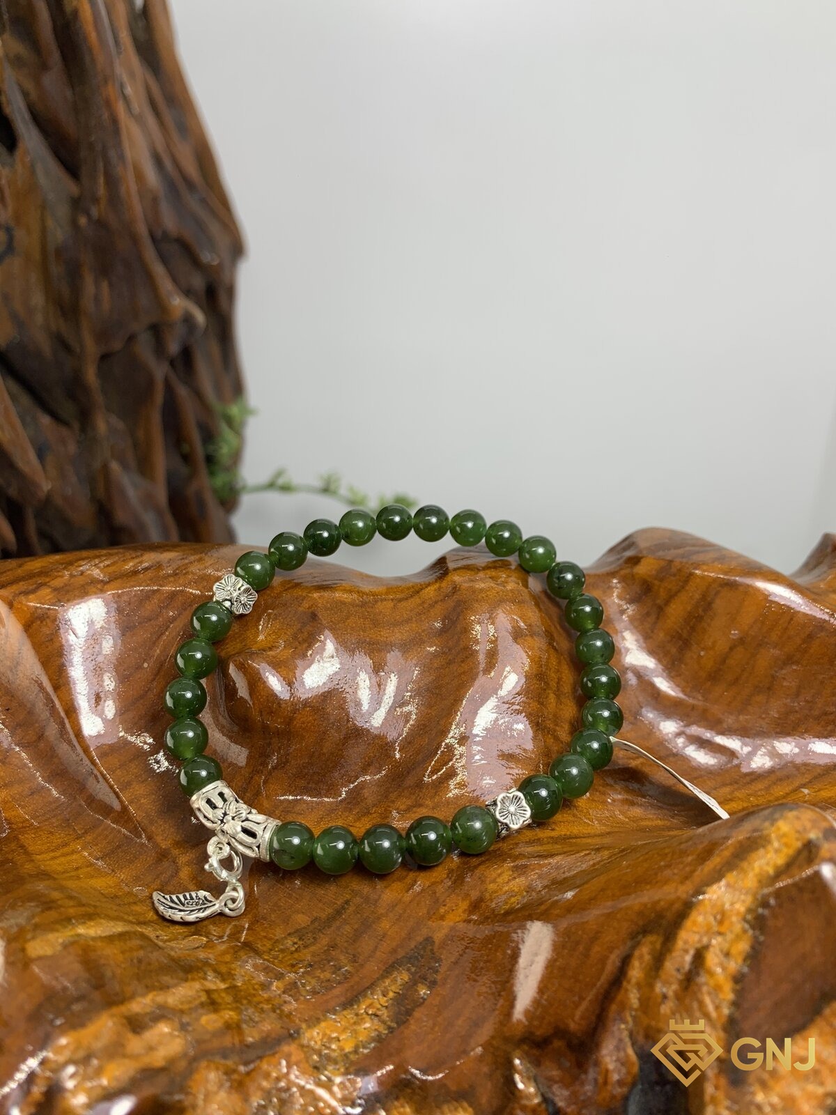 Vòng tay ngọc bích nephrite charm lá bạc S925 — ảnh chính diện trên đế gỗ, ngọc bích tự nhiên xanh rêu