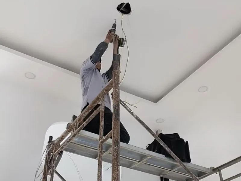 Thợ kỹ thuật khoan cấy ty ren chịu lực lắp đặt quạt trần có đèn trên trần thạch cao