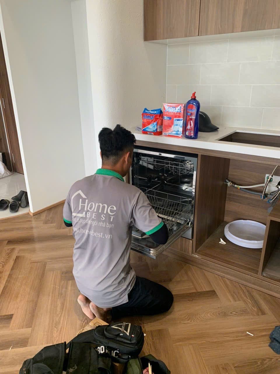 Kỹ thuật viên kiểm tra đường ống và máy rửa chén cạnh khoang tủ chậu rửa