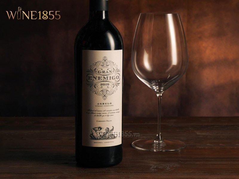 Chai rượu Gran Enemigo Agrelo Cabernet Franc kèm ly vang trống trên nền gỗ tối màu sang trọng
