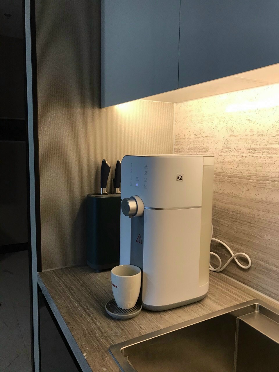 Máy lọc nước màu trắng đặt trên mặt bếp cạnh chậu rửa tại công trình HAPA ở Đống Đa