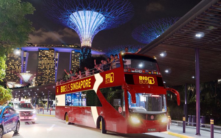 Du khách trên xe Big Bus Singapore khám phá thành phố về đêm trong tour nội địa Singapore với phông nền là các siêu cây Gardens by the Bay được thắp sáng rực rỡ và tòa nhà Marina Bay Sands phía sau