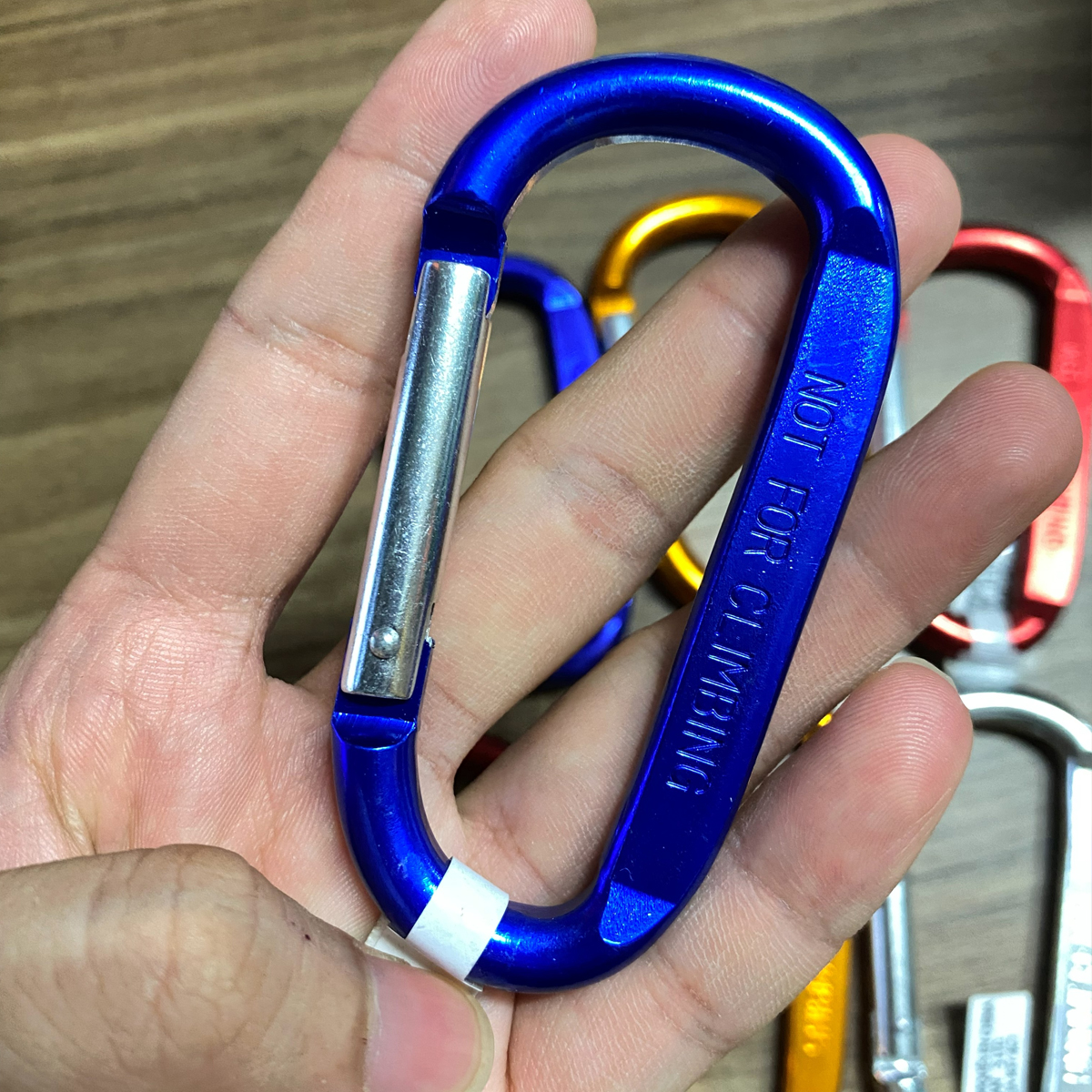 Tay người cầm nhiều móc khóa carabiner Coghlans nhiều màu móc vào nhau