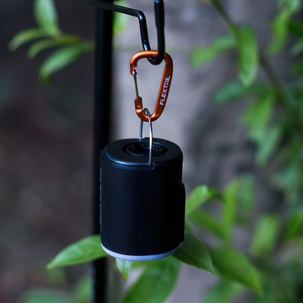 Móc khóa carabiner Flextail màu cam treo một vật hình trụ màu đen trên cây ngoài trời
