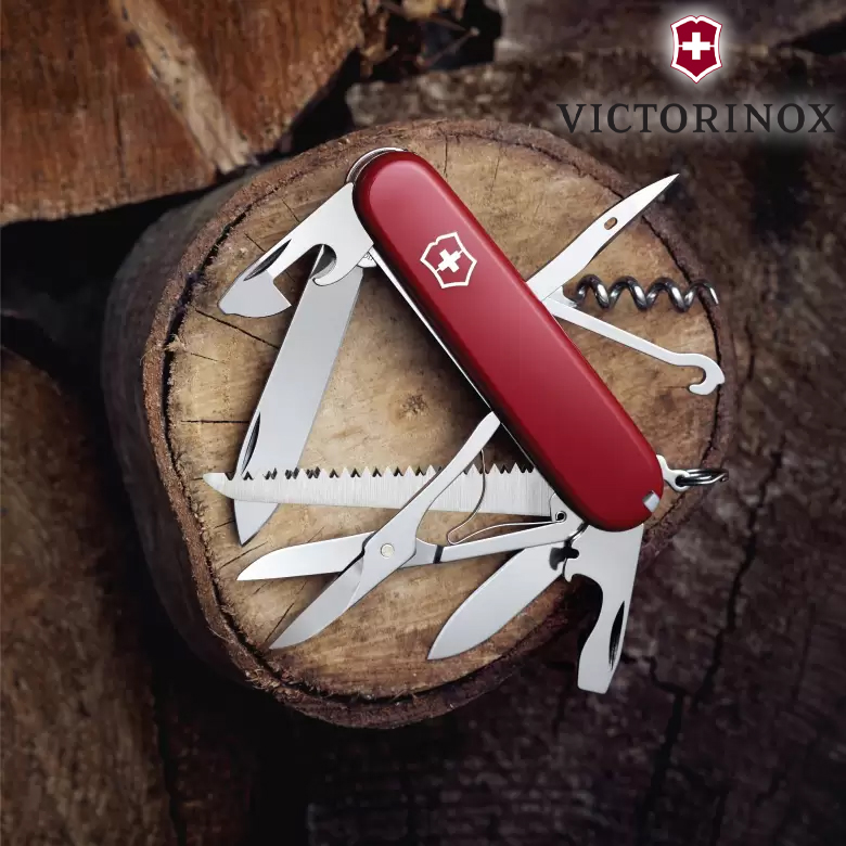 Dao đa năng Victorinox Huntsman đỏ đặt trên khúc gỗ ngoài trời, mở vài lưỡi