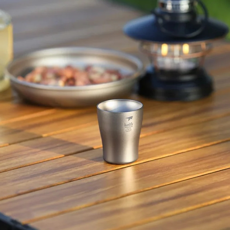 Ly Uống Rượu Keith Titanium Wine Cup 10ml một ly trên bàn gỗ cạnh đĩa hạt và đèn lồng