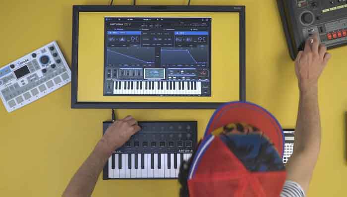 Phần mềm Synth Arturia CZ V hình đang miêu tả có người đang đặt laptop và cái thiết bị chơi nhạc gòm midi với kết nối với phầm mềm và đặt trên bàn để chơi