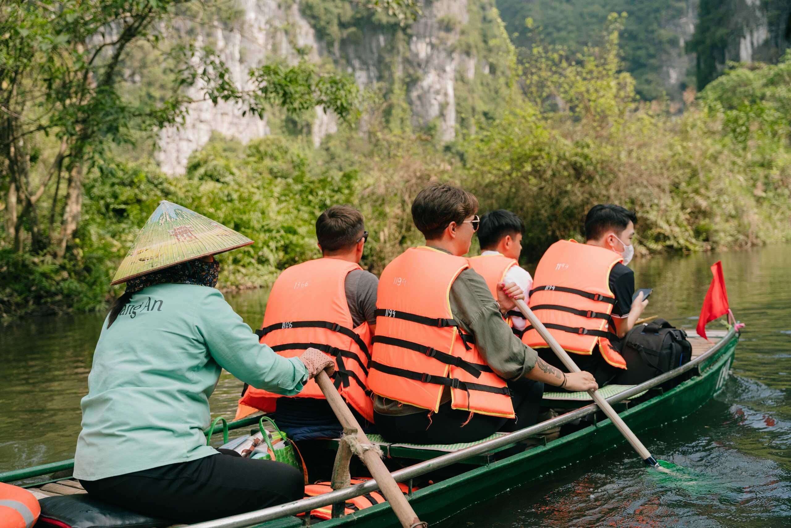 A local rower guiding visitors in orange life jackets through Tràng An