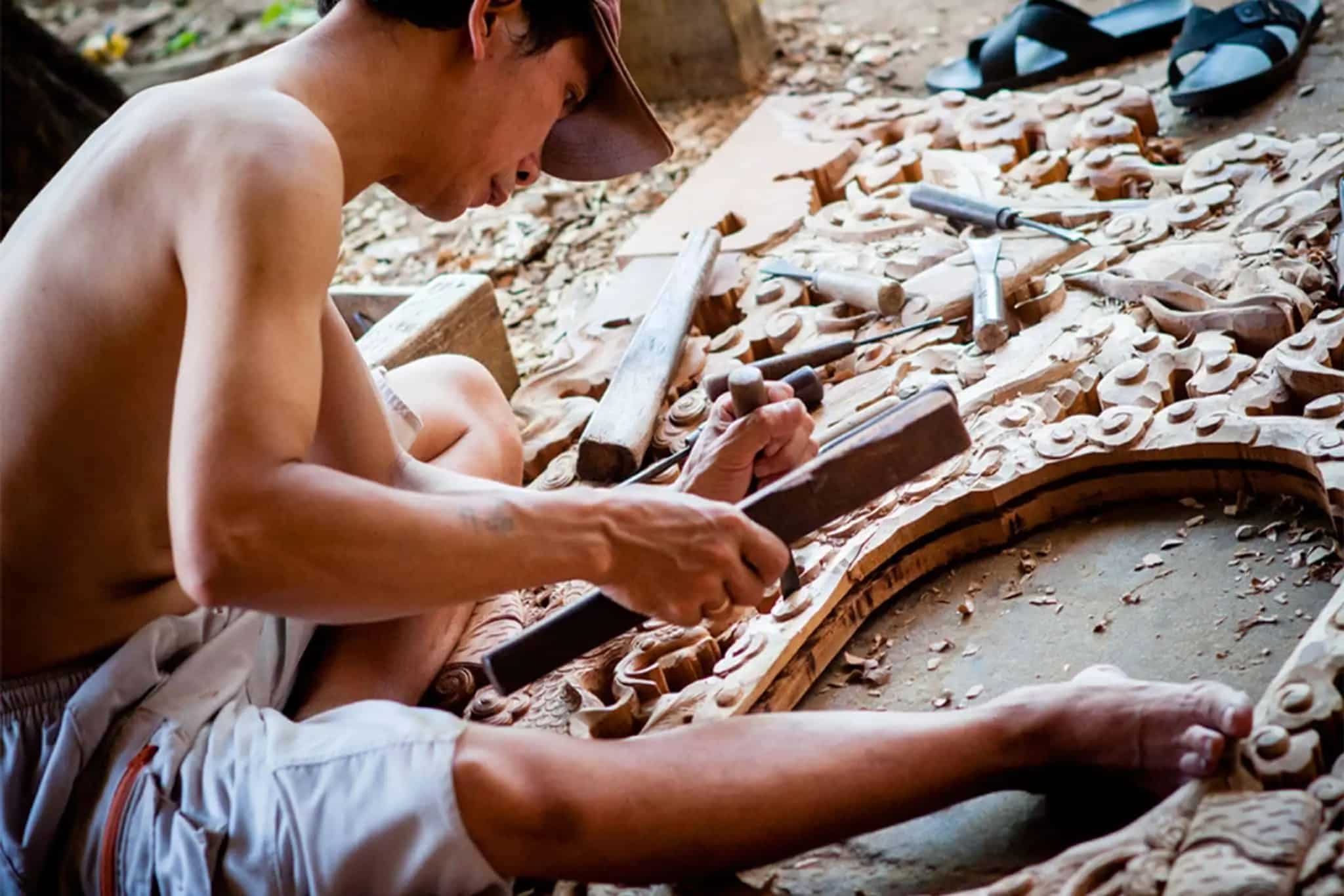 A skilled artisan carefully carves intricate patterns into a wooden panel using traditional hand tools.