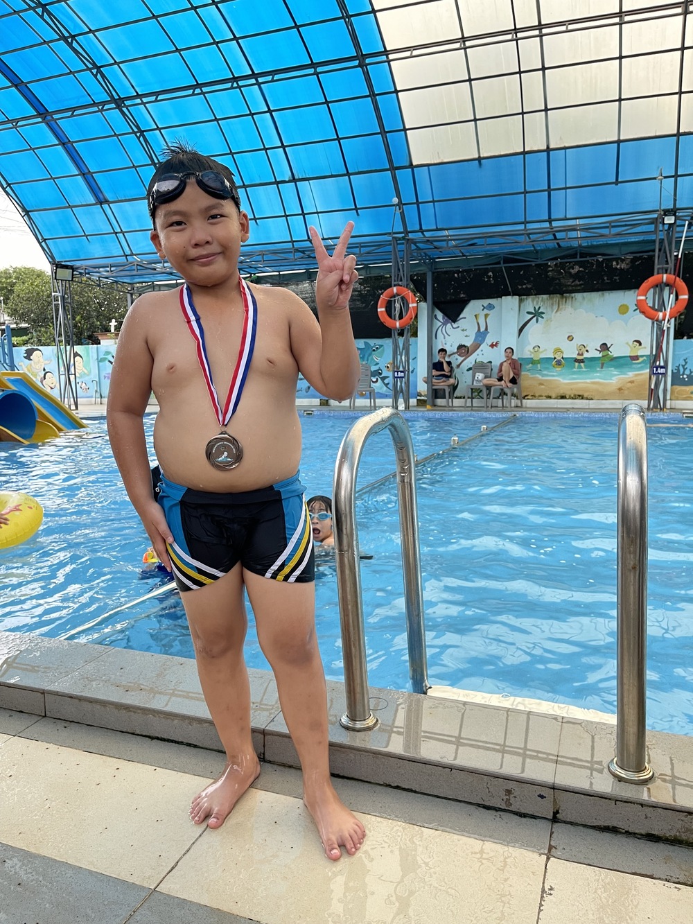 Bạn Thành nhận huy chương hoàn tất chương trình học bơi ếch căn bản mùa Hè