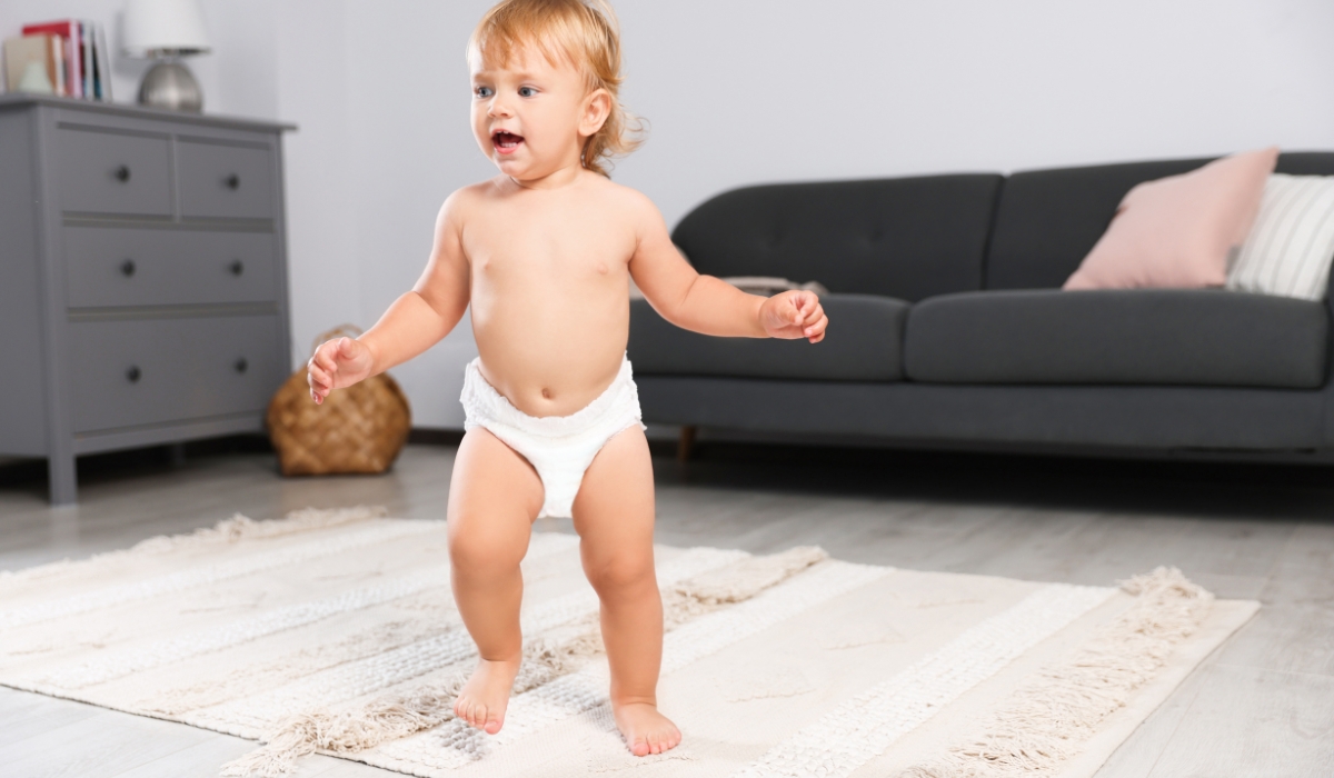 Trẻ nhỏ đứng trên thảm mềm trong phòng khách, chuẩn bị bước đi, thể hiện sự an toàn khi tập đi trên nền không trơn trượt