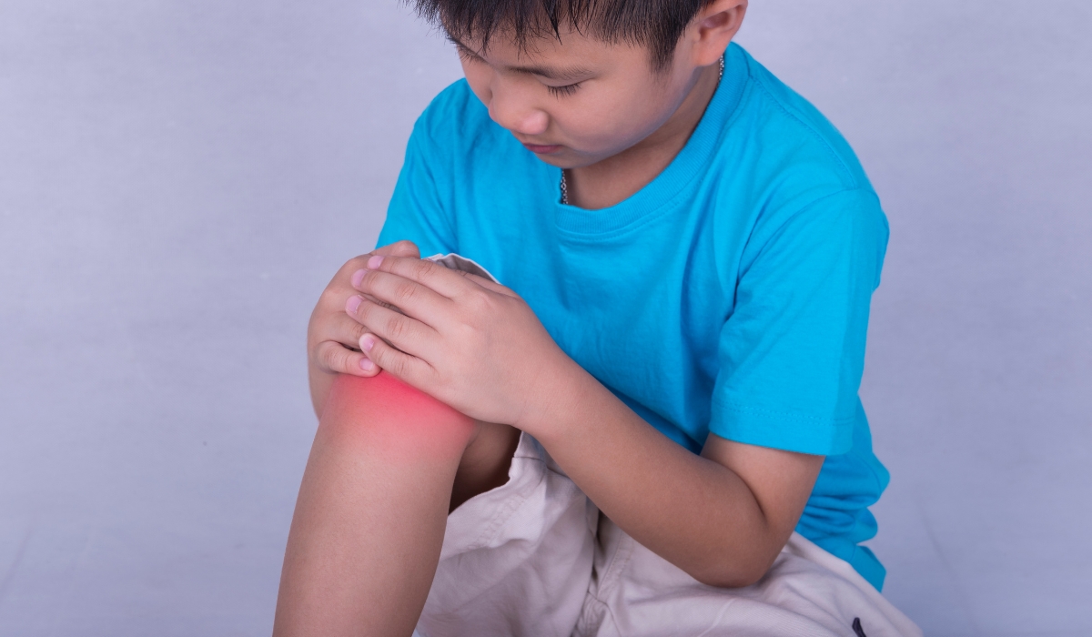 Cậu bé đang ôm đầu gối, biểu thị cảm giác đau do viêm khớp chân, thể hiện dấu hiệu của viêm khớp thiếu niên tự phát ở trẻ em