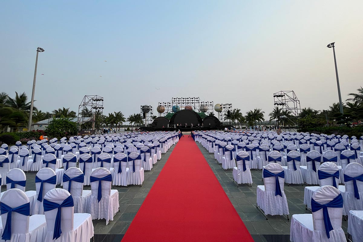 Hàng trăm ghế Banquet áo trắng nơ xanh bố trí hướng về sân khấu ngoài trời