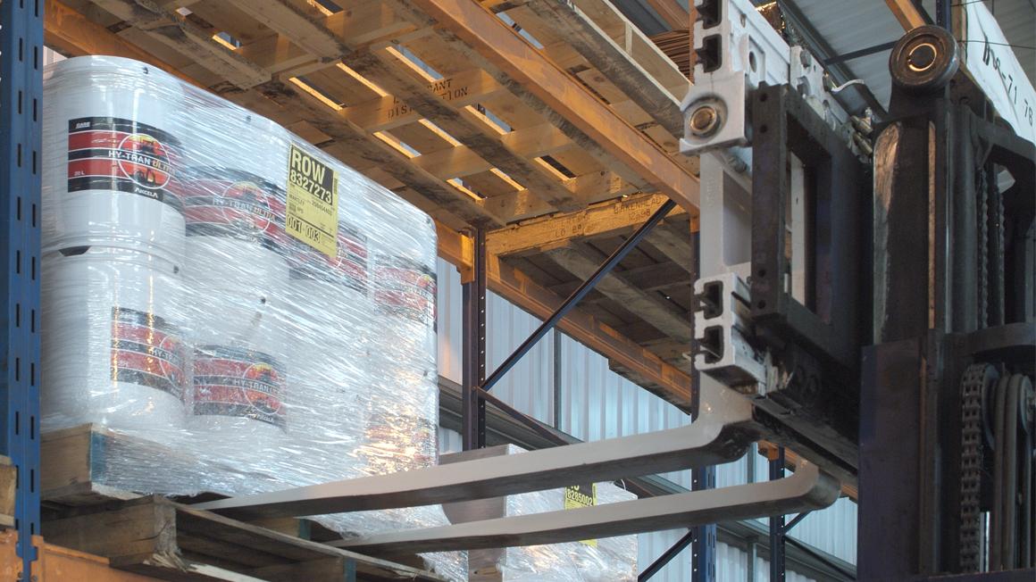 Xe nâng điện gắn bộ kẹp càng nâng pallet Pallet Fork Clamp đang giữ chặt khối hàng hóa xếp chồng cao di chuyển trong hành lang kho