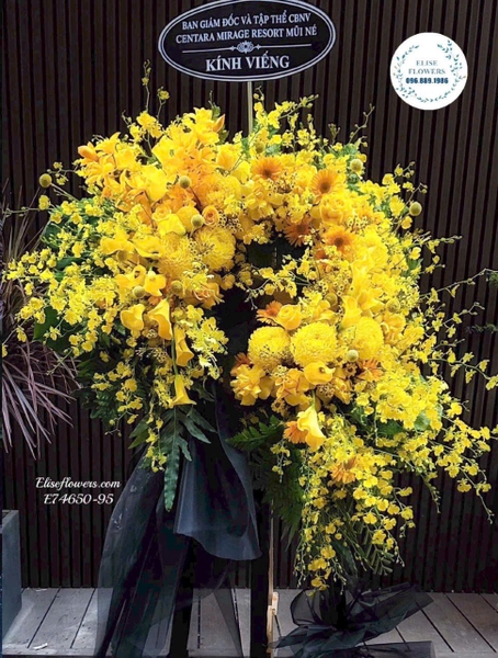 Kệ vòng hoa chia buồn tone vàng phối lá xanh và vải đen | Elise Flowers