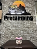 Áo len bọc bình gas mini hình mèo trắng đặt trên bàn, phía sau bảng hiệu Procamping
