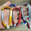 Nhiều móc khóa carabiner Coghlans màu vàng, đỏ, xanh móc chồng lên nhau trên tay, nền gỗ