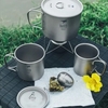 Bộ ấm và ca titanium Keith bày cùng quả lọc trà, lá trà khô và hoa vàng trên nền cỏ
